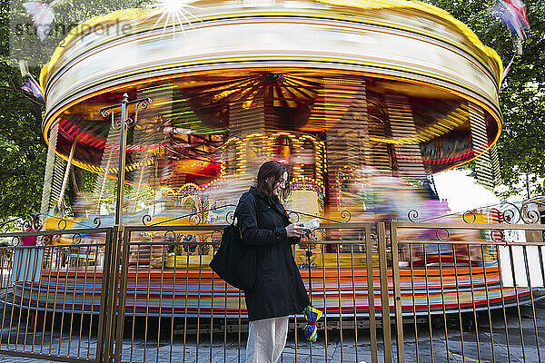 Woman standing in front of carousel at amusement park