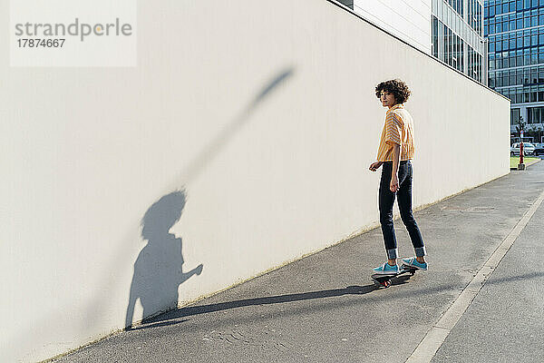 Frau fährt an sonnigem Tag auf Fußweg an der Mauer Skateboard