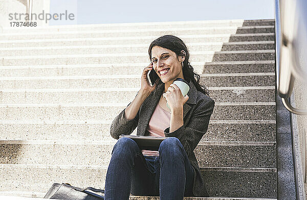 Glückliche Transgender-Geschäftsfrau  die auf einer Treppe sitzt und mit dem Handy spricht