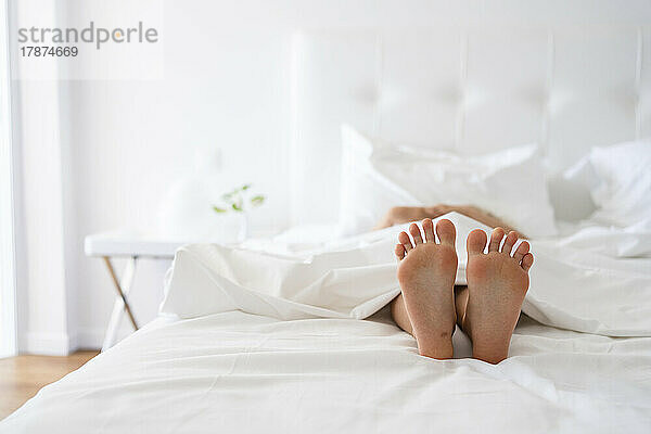 Füße eines Mädchens unter einer Decke im Bett