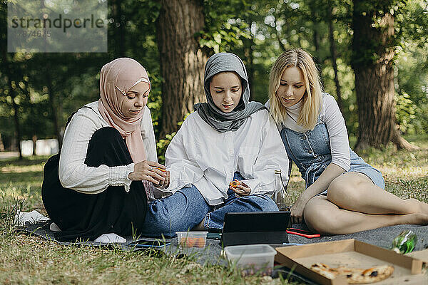 Junge Freunde schauen sich im Park Videos auf einem Tablet-PC an