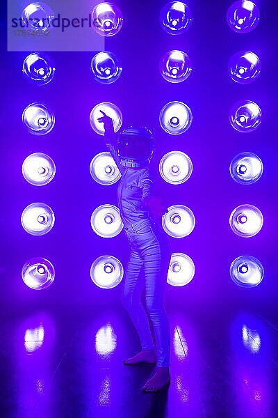 Frau mit Weltraumhelm tanzt vor Neonbeleuchtung