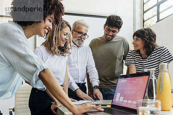 Lächelnde  gemischtrassige Kollegen  die bei einer Besprechung im Büro am Laptop diskutieren