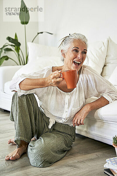 Woman laughing with coffee mug sitting by sofa