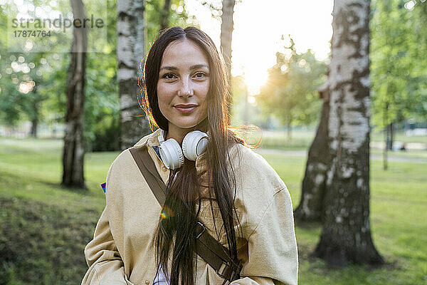 Lächelnde Frau mit Kopfhörern steht im Park