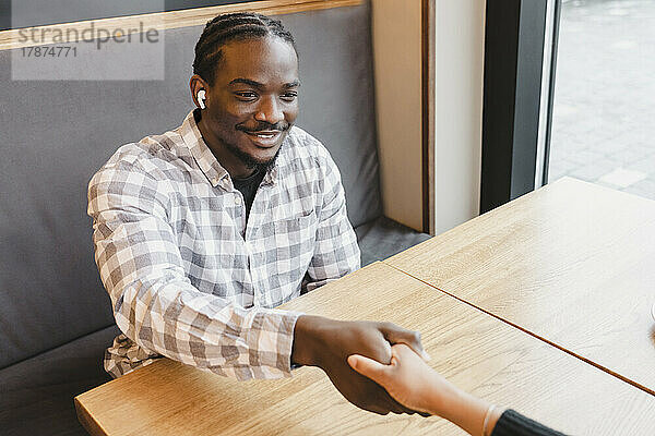 Happy young businessman shaking hand with businesswoman at cafe