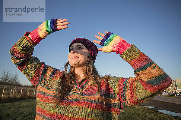Lächelnde Frau mit Regenbogenhandschuhen  die an einem sonnigen Tag die Augen schützen