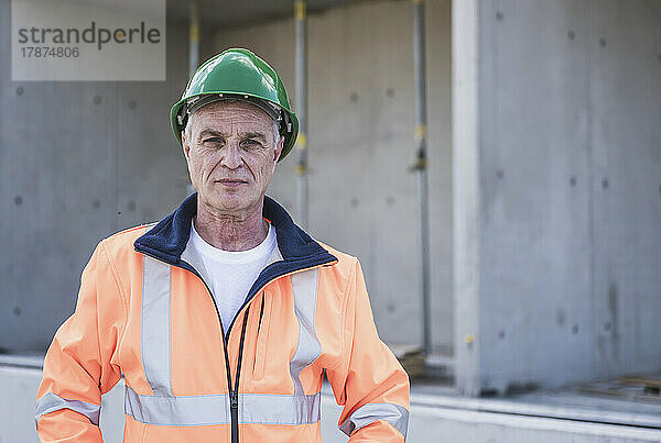 Selbstbewusster Bauarbeiter mit reflektierender Kleidung und Schutzhelm steht auf der Baustelle