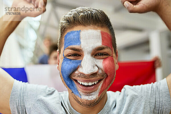 Glücklicher Fan mit aufgemalter französischer Flagge im Gesicht im Stadion