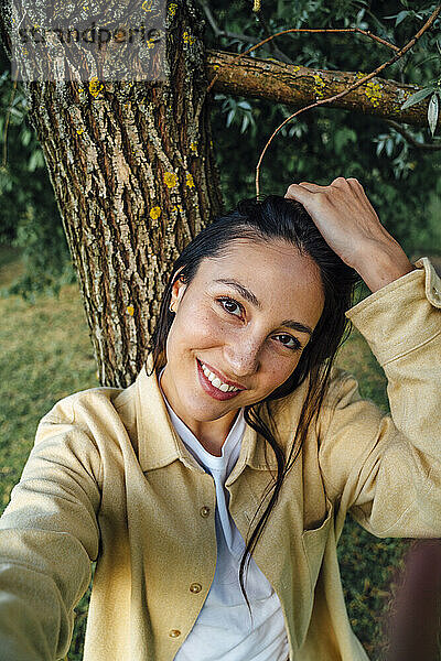 Glückliche Frau macht ein Selfie vor einem Baum im Park