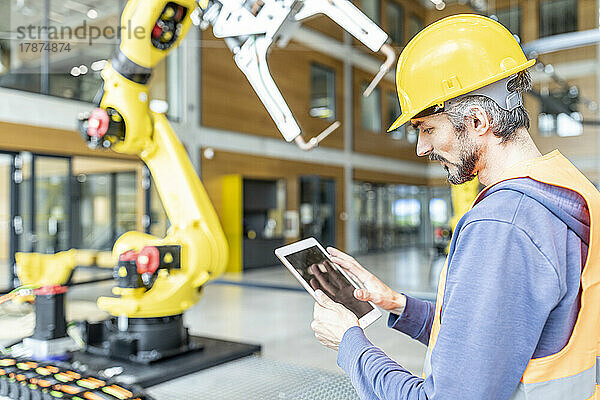 Facharbeiter steuert Roboterarm mit digitalem Tablet