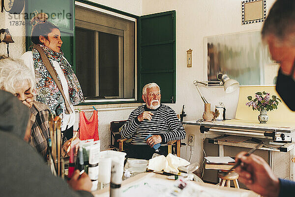 Nachdenklicher älterer Mann sitzt mit Künstlern zu Hause