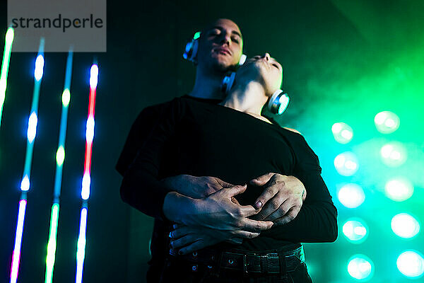 Couple wearing headphones embracing in front of glowing lights