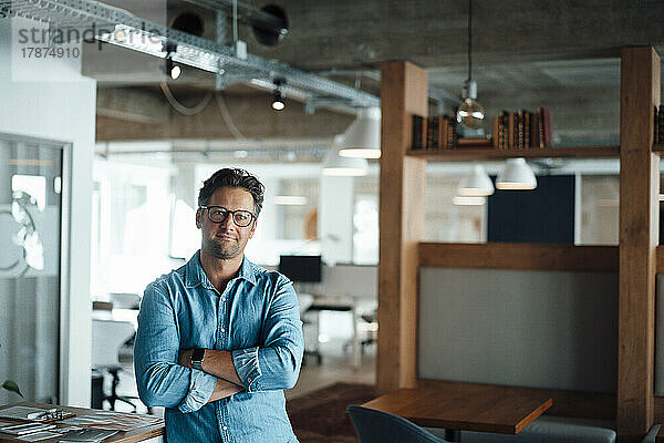 Smiling mature businessman standing with arms crossed in office