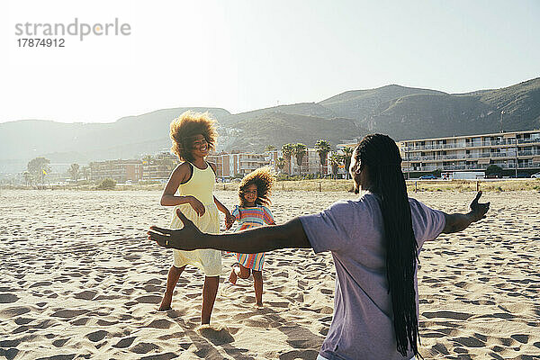 Töchter rennen mit ausgestreckten Armen am Strand auf den Vater zu