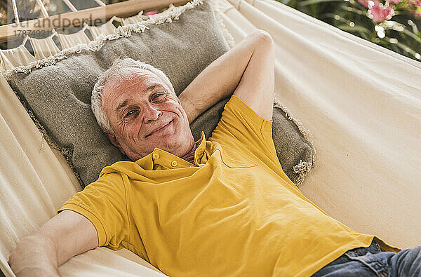 Smiling retired senior man with hand behind head relaxing in hammock