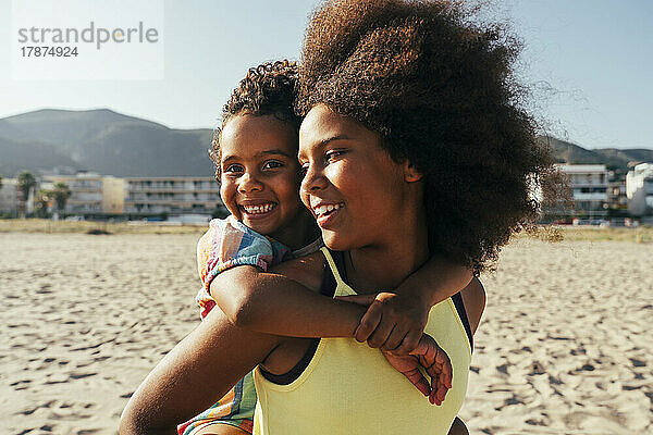 Lächelndes Mädchen huckepack  Schwester am Strand