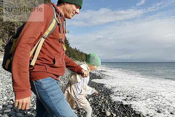 Verspielter Vater und Tochter gehen am Strand in Richtung Meer