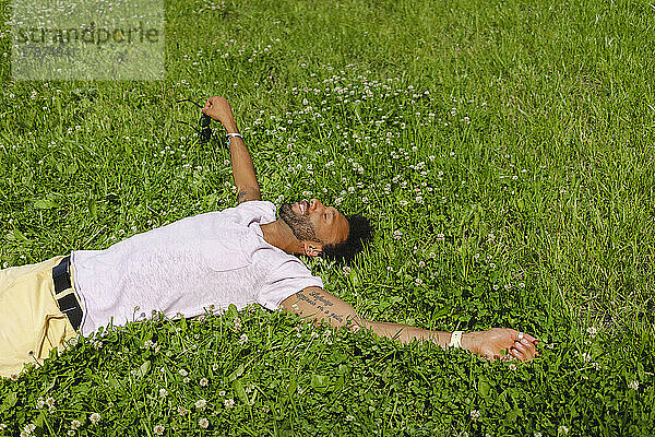 Lächelnder Mann mit ausgestreckten Armen entspannt sich im Gras im Park