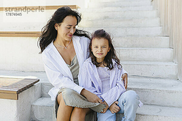 Lächelnde Frau mit Tochter  die auf Stufen sitzt
