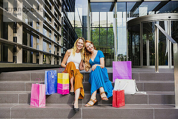 Fröhliche Freunde mit Einkaufstüten auf der Treppe vor dem Einkaufszentrum