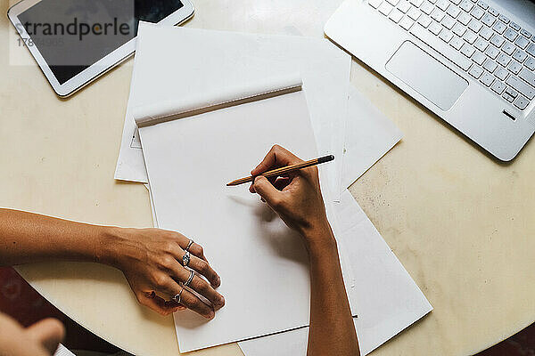 Hand eines Modedesigners hält Bleistift auf Skizzenblock am Schreibtisch