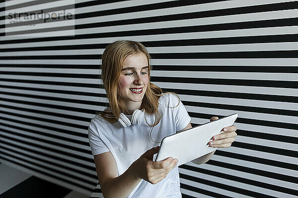 Schönes Teenager-Mädchen mit Tablet-PC vor gestreifter Wand
