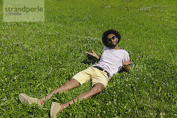 Mann liegt auf Gras und gestikuliert im Park