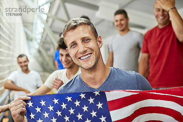 Glücklicher Mann hält amerikanische Flagge mit Freunden bei Sportveranstaltung im Stadion