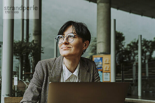 Lächelnde Geschäftsfrau mit Laptop sitzt im Straßencafé