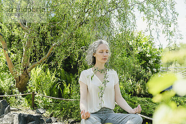 Frau meditiert vor Bäumen im Park