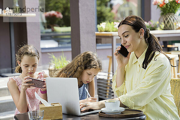 Freelancer using laptop and smart phone by daughters at sidewalk cafe