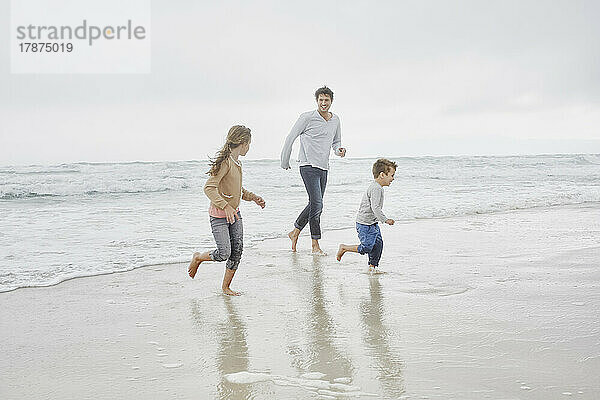 Vater läuft mit Sohn und Tochter am Strand