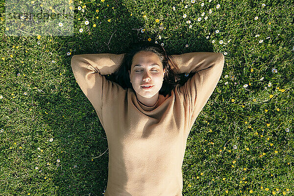Junge Frau mit den Händen hinter dem Kopf liegt im Gras im Park