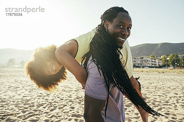 Glücklicher Mann trägt Tochter auf der Schulter am Strand