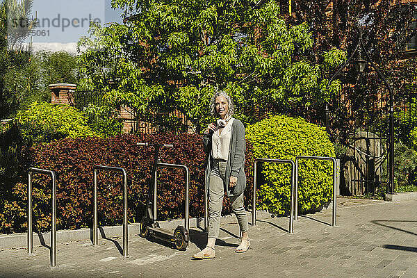 Lächelnde Frau läuft an einem sonnigen Tag am Fahrradparkplatz vorbei