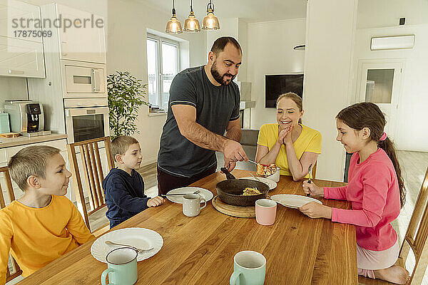 Lächelnder Vater serviert der Familie zu Hause Frühstück