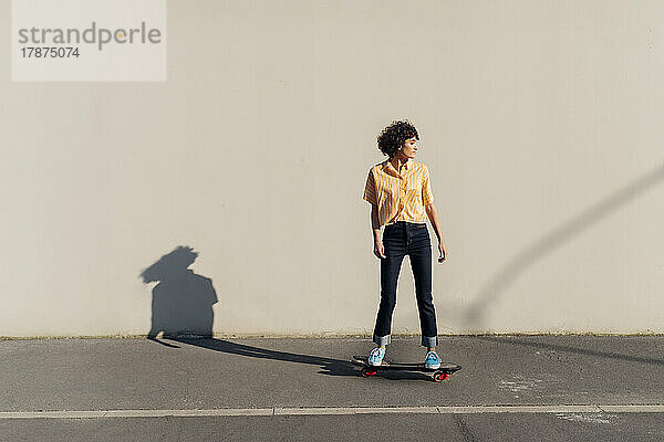 Frau fährt an einem sonnigen Tag vor der Wand Skateboard