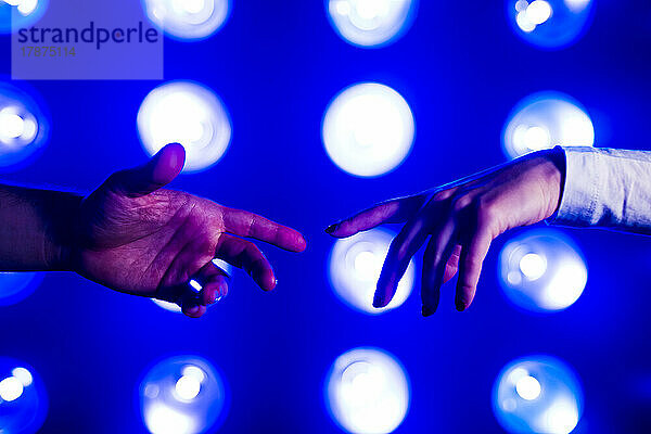 Hände eines Paares greifen vor beleuchteten Lichtern aufeinander zu