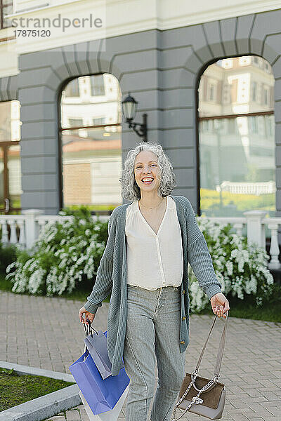 Glückliche Frau mit Einkaufstüten vor dem Gebäude