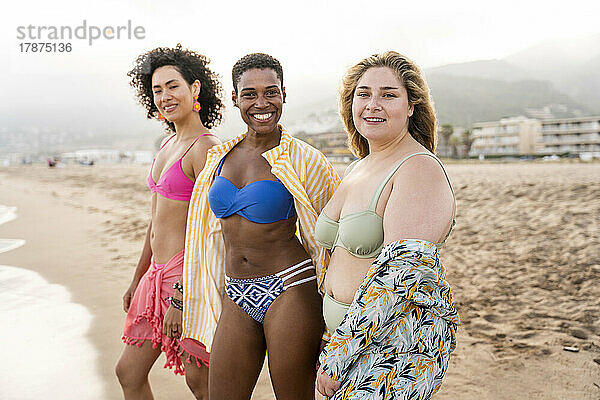 Fröhliche Freunde in Badebekleidung stehen am Strand