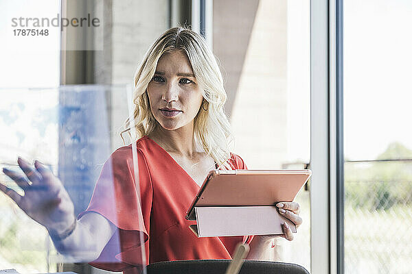Geschäftsfrau hält Tablet-PC und berührt transparenten Bildschirm im Büro