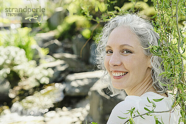Glückliche Frau mit grauen Haaren neben Pflanzen an einem sonnigen Tag