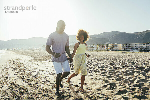 Vater und Tochter laufen an einem sonnigen Tag am Strand