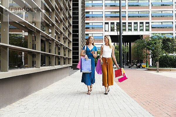 Freunde mit Einkaufstüten gehen gemeinsam auf dem Fußweg spazieren
