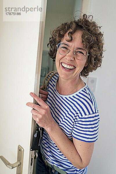 Cheerful woman wearing eyeglasses standing with house key by door