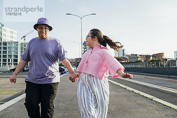Bruder und Schwester mit Down-Syndrom halten sich an den Händen und gehen auf der Straße