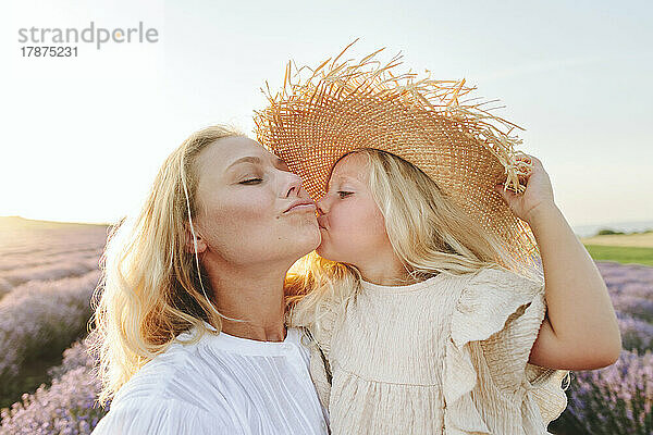 Girl wearing hat kissing mother at field