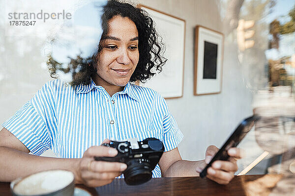 Lächelnde Frau mit Kamera und Smartphone am Tisch im Café