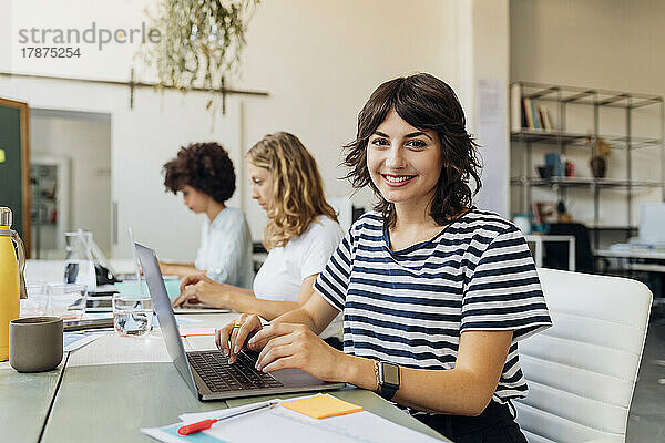 Lächelnde Geschäftsfrau mit Laptop am Arbeitsplatz